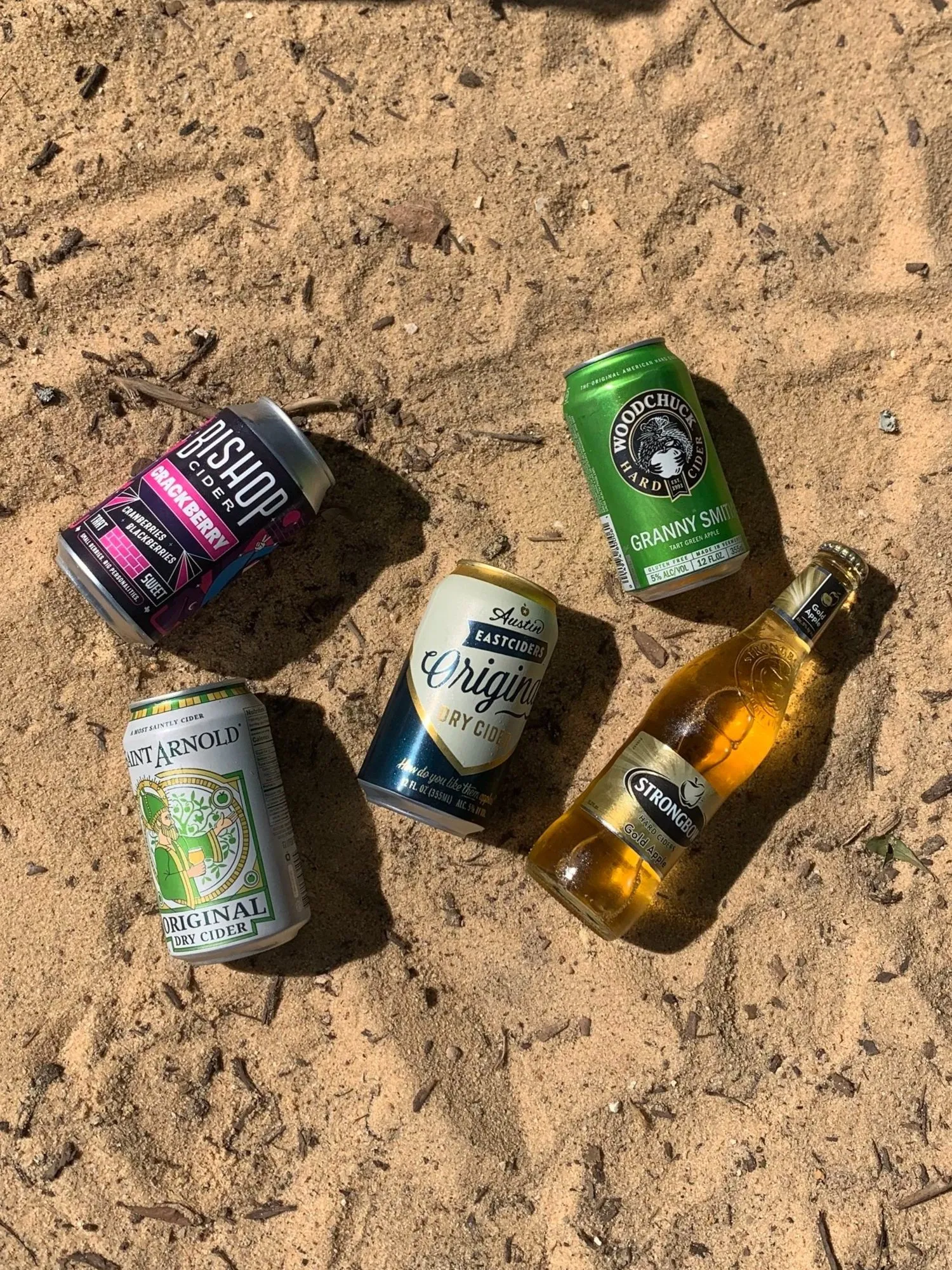 Cans and bottles of cider laid out in the sand