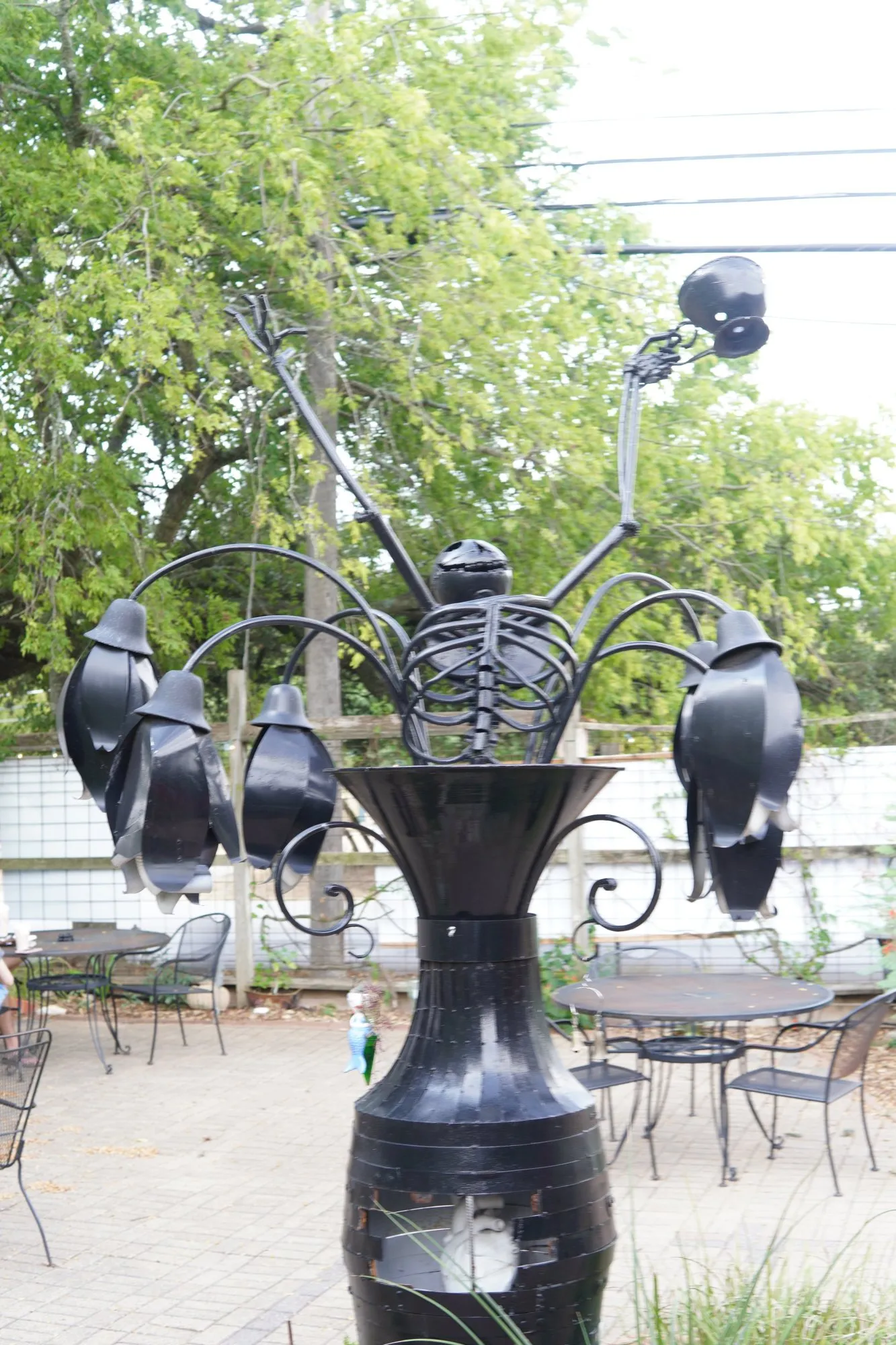 The courtyard sculpture: a metal skeleton rising from an urn, holding a coffee cup