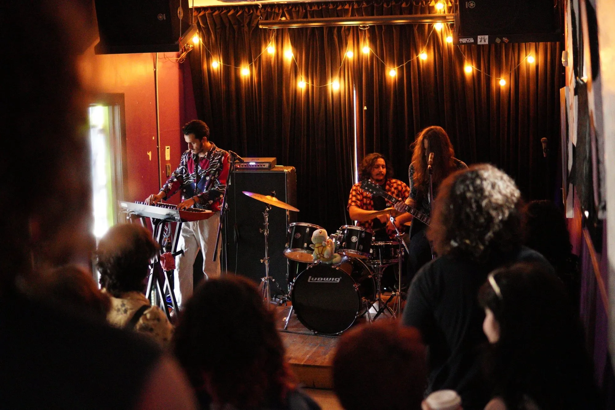 A band playing in the stage room under string lights, the crowd up close